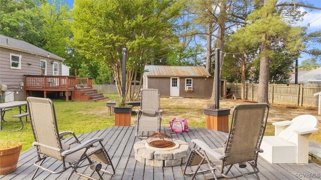 Wooden terrace with an outdoor fire pit, an outdoor structure, a fenced backyard, a lawn, and stairs | Image 32