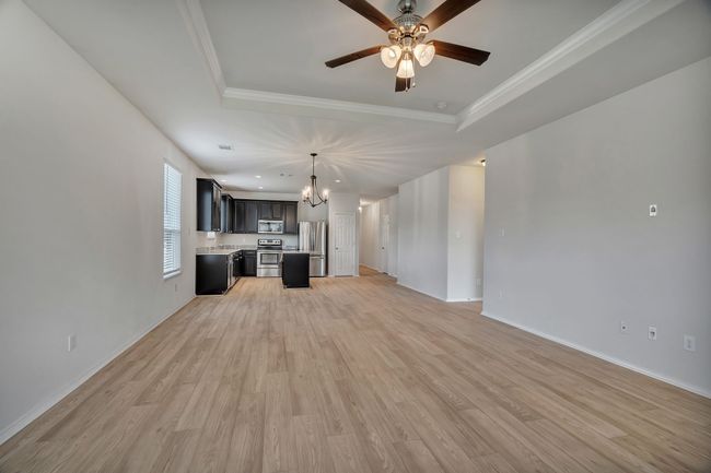 Unfurnished living room with a raised ceiling, ceiling fan, light wood finished floors, a chandelier, and ornamental molding | Image 16