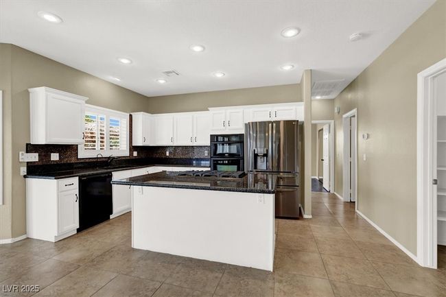 Kitchen featuring black appliances, white cabinetry, a center island, light tile patterned flooring, and tasteful backsplash | Image 13