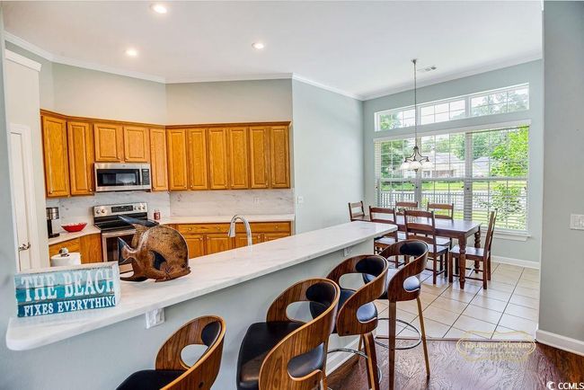 Kitchen featuring appliances with stainless steel finishes, crown molding, brown cabinetry, a chandelier, and a breakfast bar | Image 13