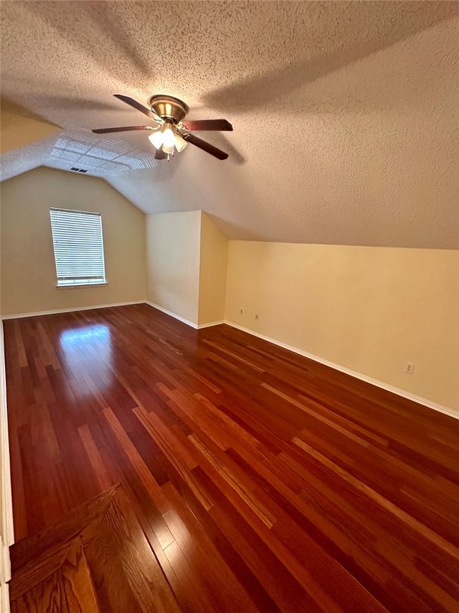 Additional living space featuring a textured ceiling, wood finished floors, lofted ceiling, and ceiling fan | Image 16