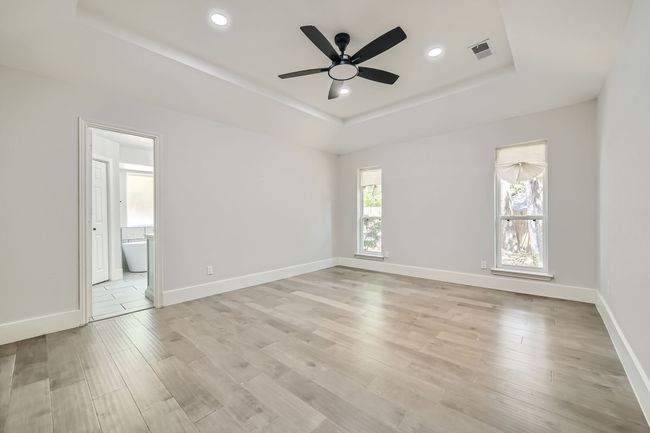 Empty room with light wood-style flooring, visible vents, a tray ceiling, recessed lighting, and a ceiling fan | Image 16