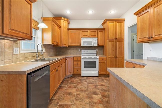 Kitchen featuring a sink, white appliances, light countertops, decorative light fixtures, and tasteful backsplash | Image 13