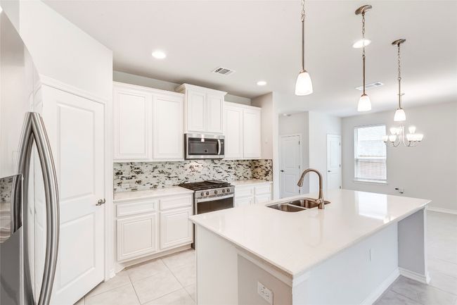 Kitchen featuring stainless steel appliances, a sink, tasteful backsplash, white cabinetry, and a kitchen island with sink | Image 12