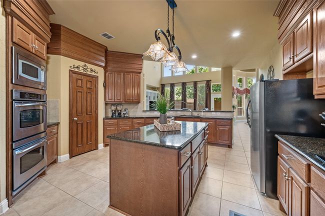 Kitchen with stainless steel appliances, a center island, light tile patterned floors, recessed lighting, and dark stone counters | Image 17