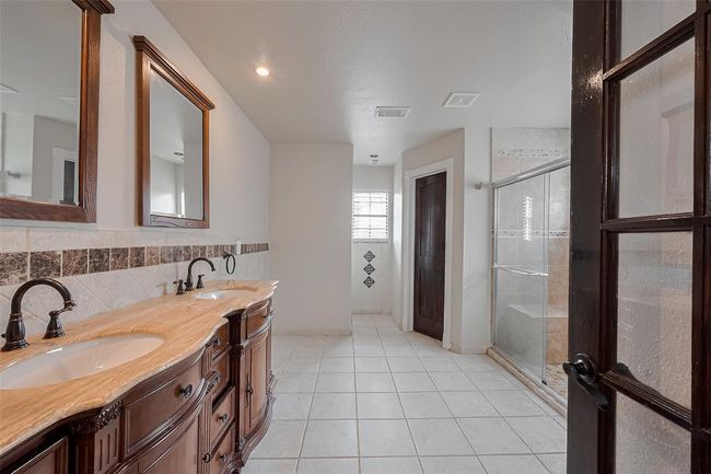 The luxurious primary bathroom features double vanities with elegant granite countertops, framed mirrors, and classic oil-rubbed bronze fixtures. Tile accents and warm wood cabinetry elevate the overall design. | Image 26