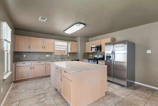 This spacious kitchen features light wood cabinetry, stainless steel appliances, a gas range, and an oversized center island with additional storage. Neutral-toned tile flooring, ample counter space, and a large window over the sink add to the bright and functional layout, perfect for everyday living and entertaining. | Image 9