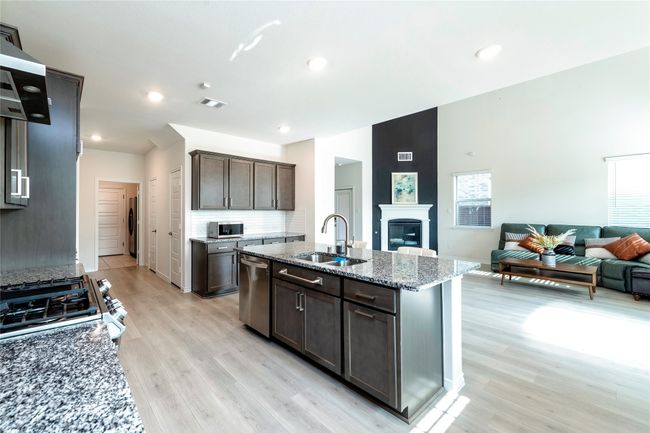 Kitchen with light stone countertops, open floor plan, ventilation hood, light wood finished floors, and a kitchen island with sink | Image 9