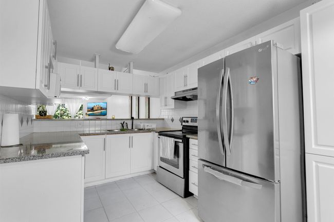 Kitchen featuring stainless steel appliances, white cabinets, decorative backsplash, stone counters, and light tile patterned floors | Image 6