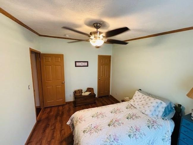 Bedroom with a textured ceiling, crown molding, a ceiling fan, and dark wood finished floors | Image 11