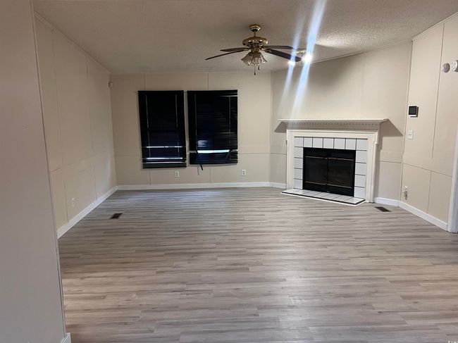 Unfurnished living room featuring a ceiling fan, wood finished floors, a textured ceiling, and a tile fireplace | Image 6