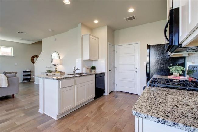 Kitchen with black appliances, a peninsula, light wood-style flooring, white cabinets, and light stone counters | Image 11