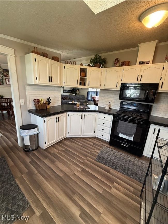 Kitchen featuring dark wood-style floors, a textured ceiling, tasteful backsplash, stove, and crown molding | Image 11