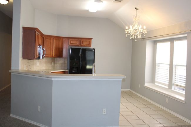 Kitchen with light tile patterned floors, black refrigerator with ice dispenser, a notable chandelier, brown cabinets, and stainless steel microwave | Image 16