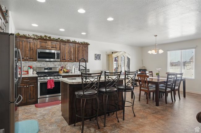 Kitchen with recessed lighting, backsplash, a kitchen island with sink, a kitchen bar, and appliances with stainless steel finishes | Image 16