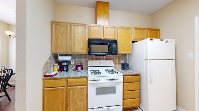 Kitchen with light brown cabinetry, white appliances, light wood finished floors, and decorative backsplash | Image 8