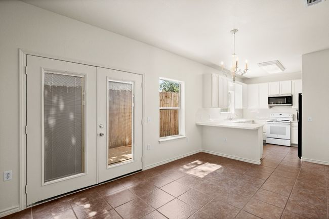 Kitchen with white range with electric stovetop, a peninsula, white cabinets, a chandelier, and hanging light fixtures | Image 4
