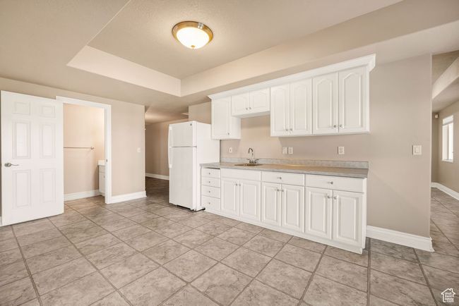 Kitchen with freestanding refrigerator, a sink, light countertops, baseboards, and a tray ceiling | Image 28