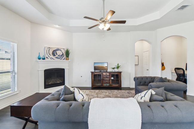 Living room with a raised ceiling, arched walkways, ceiling fan, and visible vents | Image 5