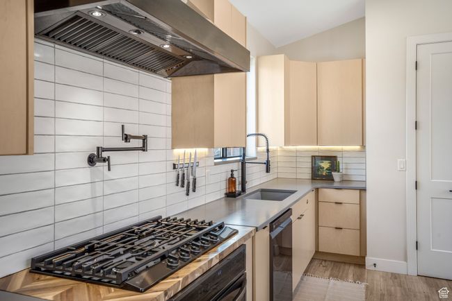 Kitchen featuring black gas cooktop, a sink, wall chimney range hood, dishwashing machine, and vaulted ceiling | Image 7