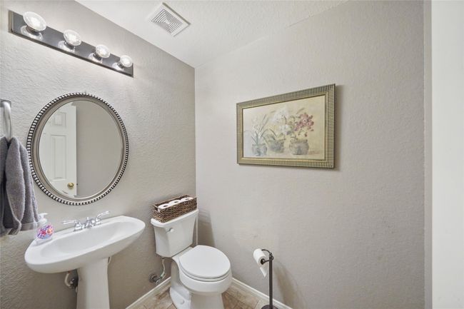 Cozy bathroom with neutral tones, featuring a pedestal sink, round mirror, and a wall-mounted light fixture. | Image 17