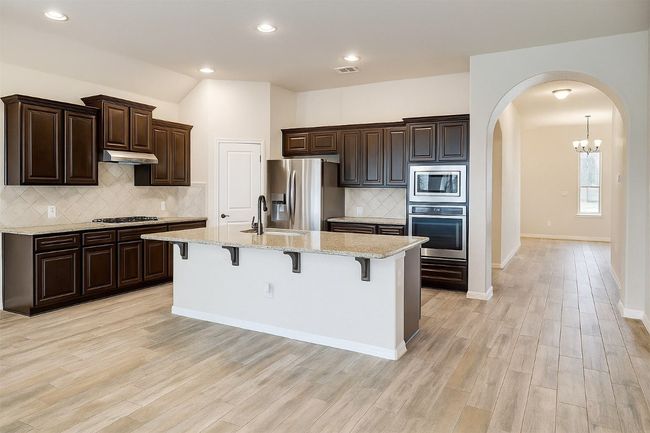 Kitchen featuring appliances with stainless steel finishes, arched walkways, under cabinet range hood, a kitchen bar, and tasteful backsplash | Image 4