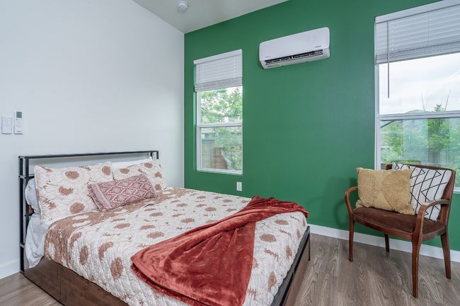 Bedroom with a wall mounted AC, wood finished floors, and baseboards. | Image 29