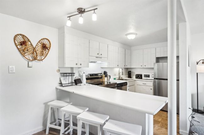 Kitchen with under cabinet range hood, stainless steel appliances, light countertops, a sink, and a peninsula | Image 10