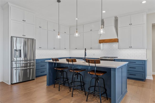 Kitchen with custom exhaust hood, light wood-type flooring, light countertops, blue cabinetry, and stainless steel appliances | Image 7