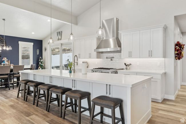 Kitchen featuring decorative backsplash, white cabinets, light wood-type flooring, vaulted ceiling, and wall chimney exhaust hood | Image 54