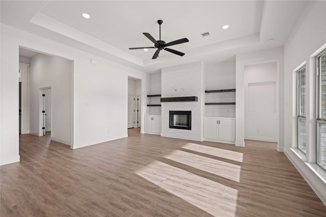 Unfurnished living room featuring a raised ceiling, a ceiling fan, light wood finished floors, a fireplace, and recessed lighting | Image 14