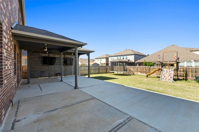 View of patio featuring ceiling fan, a privacy fenced backyard, a playground, and a trampoline | Image 27