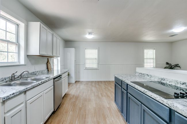 Kitchen with stainless steel dishwasher, light wood-style floors, wainscoting, black electric cooktop, and white cabinets | Image 12