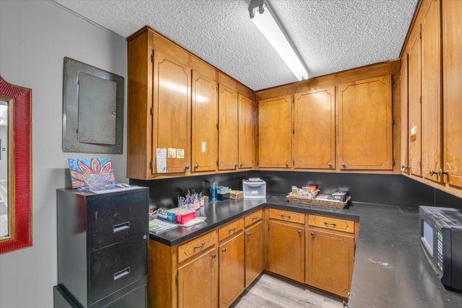 Kitchen with dark countertops, a textured ceiling, brown cabinetry, and black microwave | Image 16