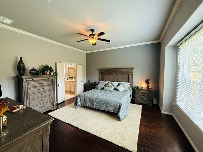 A vast primary bedroom features gleaming engineered hardwood floors, a ceiling fan, and an ensuite bathroom. | Image 19