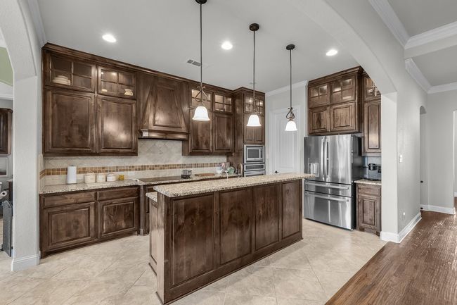 Kitchen featuring appliances with stainless steel finishes, arched walkways, premium range hood, ornamental molding, and dark brown cabinetry | Image 23