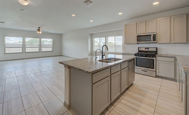 Kitchen with appliances with stainless steel finishes, a sink, backsplash, ceiling fan, and a kitchen island with sink | Image 9