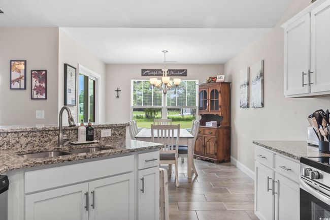 Kitchen with a chandelier, white cabinetry, light stone countertops, hanging light fixtures, and stainless steel stove | Image 12