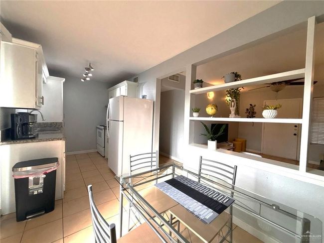 Kitchen featuring built in features, light tile patterned floors, white appliances, white cabinetry, and a sink | Image 7