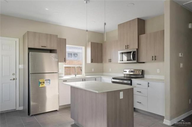 Kitchen with sink, hanging light fixtures, light tile patterned floors, a kitchen island, and stainless steel appliances | Image 4