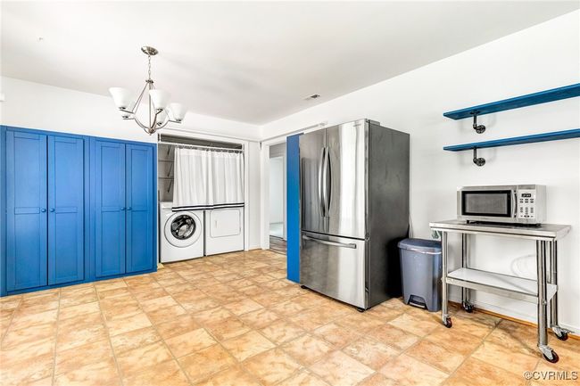 Kitchen featuring stainless steel appliances, washer and clothes dryer, blue cabinets, a chandelier, and stone finish flooring | Image 25