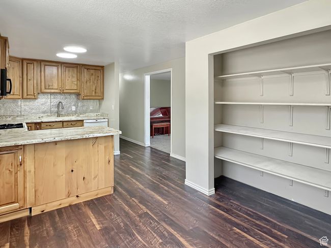 Kitchen with black microwave, light stone countertops, dark wood-style flooring, a sink, and baseboards | Image 10