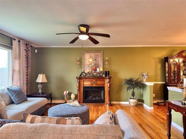 Living area featuring wood finished floors, ceiling fan, a fireplace, and ornamental molding | Image 6