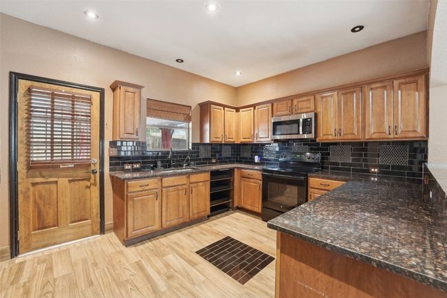 Kitchen with a sink, light wood-style floors, black electric range oven, tasteful backsplash, and stainless steel microwave | Image 8