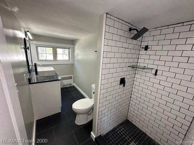 Full bath with vanity, radiator heating unit, a stall shower, and dark tile patterned floors | Image 24