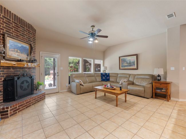 Living room featuring ceiling fan, light tile patterned flooring, baseboards, a fireplace, and vaulted ceiling | Image 7