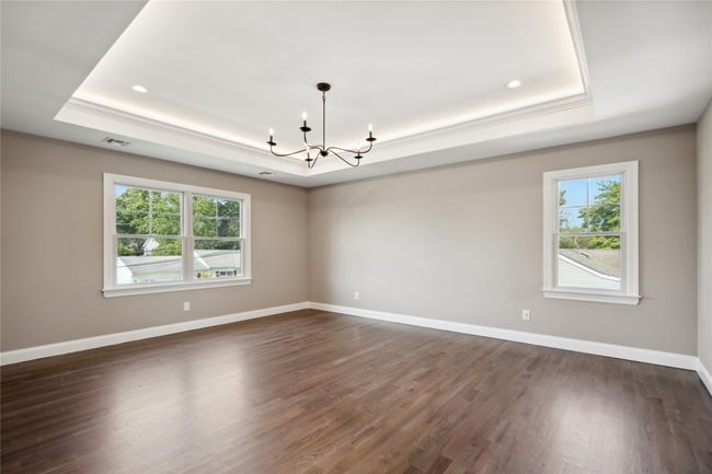 Unfurnished room with a tray ceiling, a chandelier, healthy amount of natural light, dark wood-style flooring, and ornamental molding | Image 15