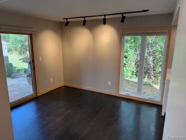 Unfurnished dining area with healthy amount of natural light, dark wood-style flooring, track lighting, and wood walls | Image 7