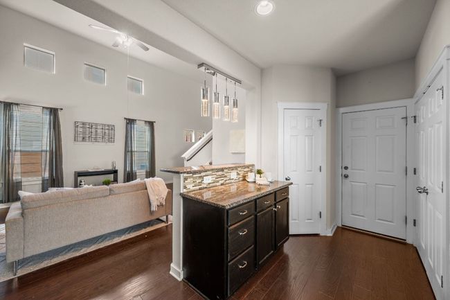 Kitchen with ceiling fan, dark wood-style floors, light stone counters, decorative light fixtures, and open floor plan | Image 14