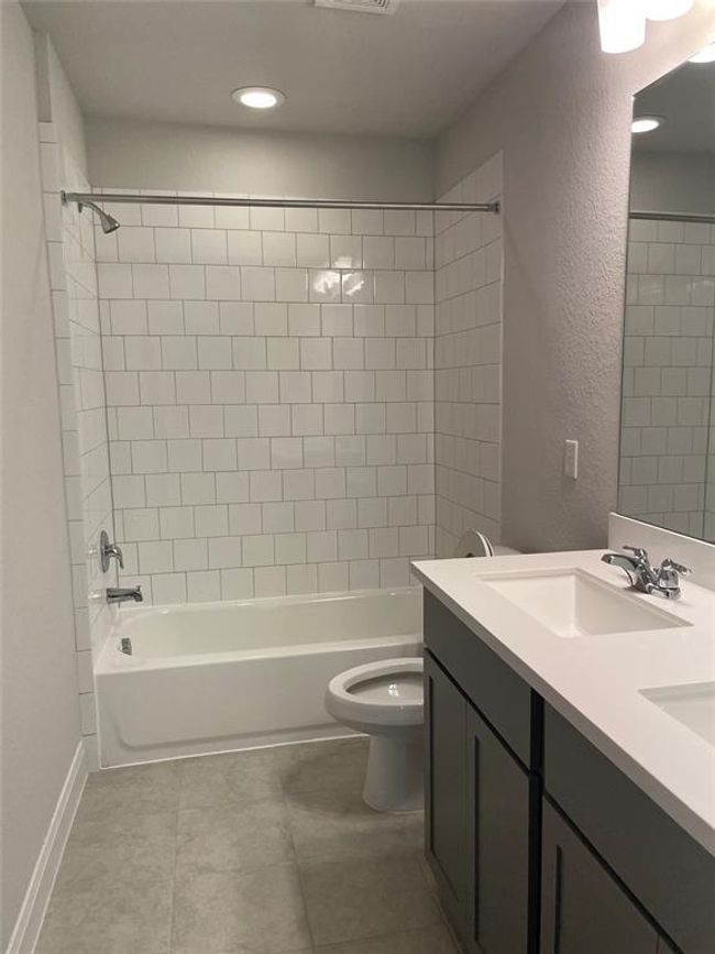 Bathroom with double vanity, bathing tub / shower combination, tile patterned flooring, a textured wall, and recessed lighting | Image 20